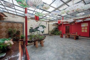 An indoor space with a glass ceiling, potted plants, and a red wall with a mural.