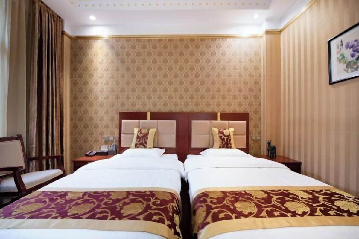 A hotel room with two beds, a nightstand, a chair, and a wall with a patterned wallpaper.
