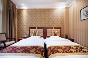 Une chambre d’hôtel avec deux lits, une table de chevet, une chaise et un mur recouvert d’un papier peint à motifs.