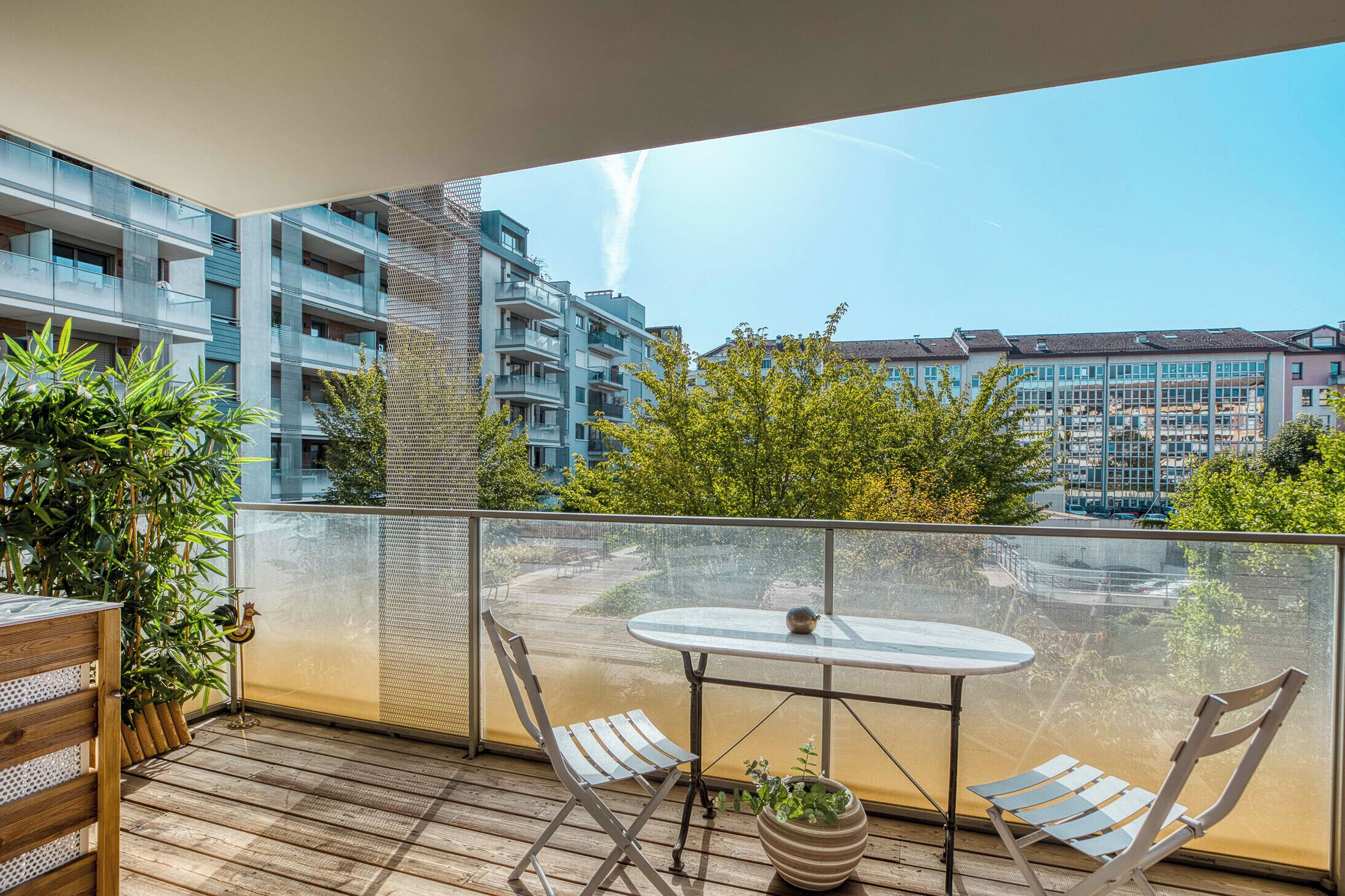A balcony with a table and chairs, a potted plant, and a view of surrounding buildings.
