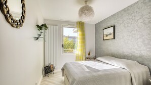 A bedroom with a bed, a mirror, a window with curtains, a picture on the wall, and a ceiling fan.