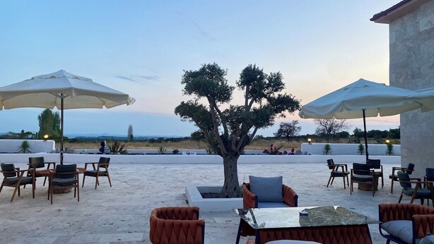 An outdoor seating area with tables and chairs, umbrellas, and a tree. - The Kirte Hotel (Eceabat)
