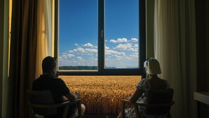 Two people seated facing a large window with a view of a golden field and a clear blue sky. - The Kirte Hotel (Eceabat)