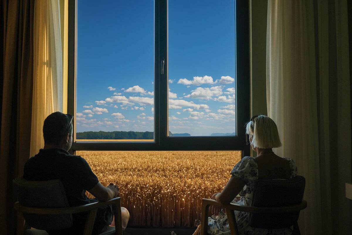 Two people seated facing a large window with a view of a golden field and a clear blue sky.