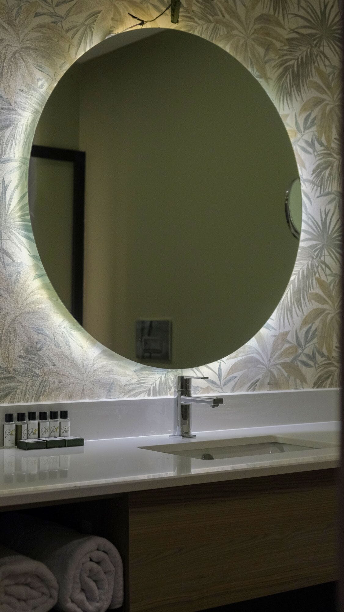 Un tocador de baño con un espejo redondo, un lavamanos y un estante con artículos de aseo.