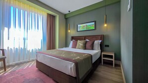 A hotel room with a large bed, a small bedside table, a chair, and a window with curtains. - The Kirte Hotel (Eceabat)