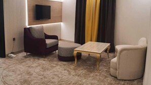 A modern living room with a flat-screen TV mounted on the wall, a sofa, a coffee table, and a chair. - Diamond corners Hotel (Madinah)