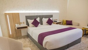 A hotel room with a large bed, a bedside table with a phone, a nightstand, a sofa, and a small table with a lamp. - Diamond corners Hotel (Madinah)