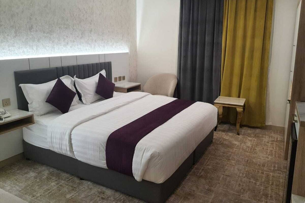 A hotel room with a bed, a nightstand, a chair, and a small table.