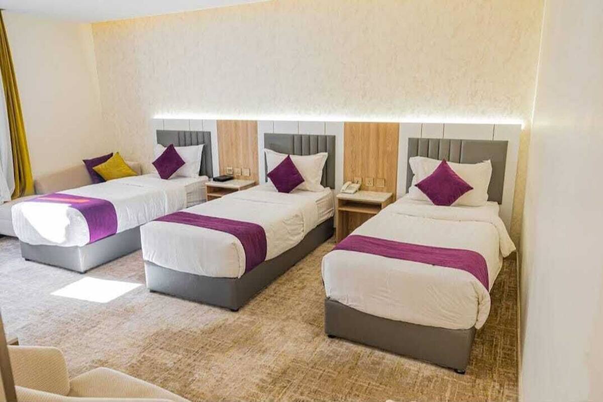 A hotel room with three beds, each with a headboard, a bedside table, and a lamp.