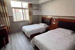 Ein Hotelzimmer mit zwei Betten, einem Schreibtisch, einem Fenster mit Vorhängen und einer Klimaanlage.