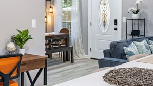 Un soggiorno moderno con zona pranzo, una porta bianca con pannello di vetro decorativo e un lampadario.