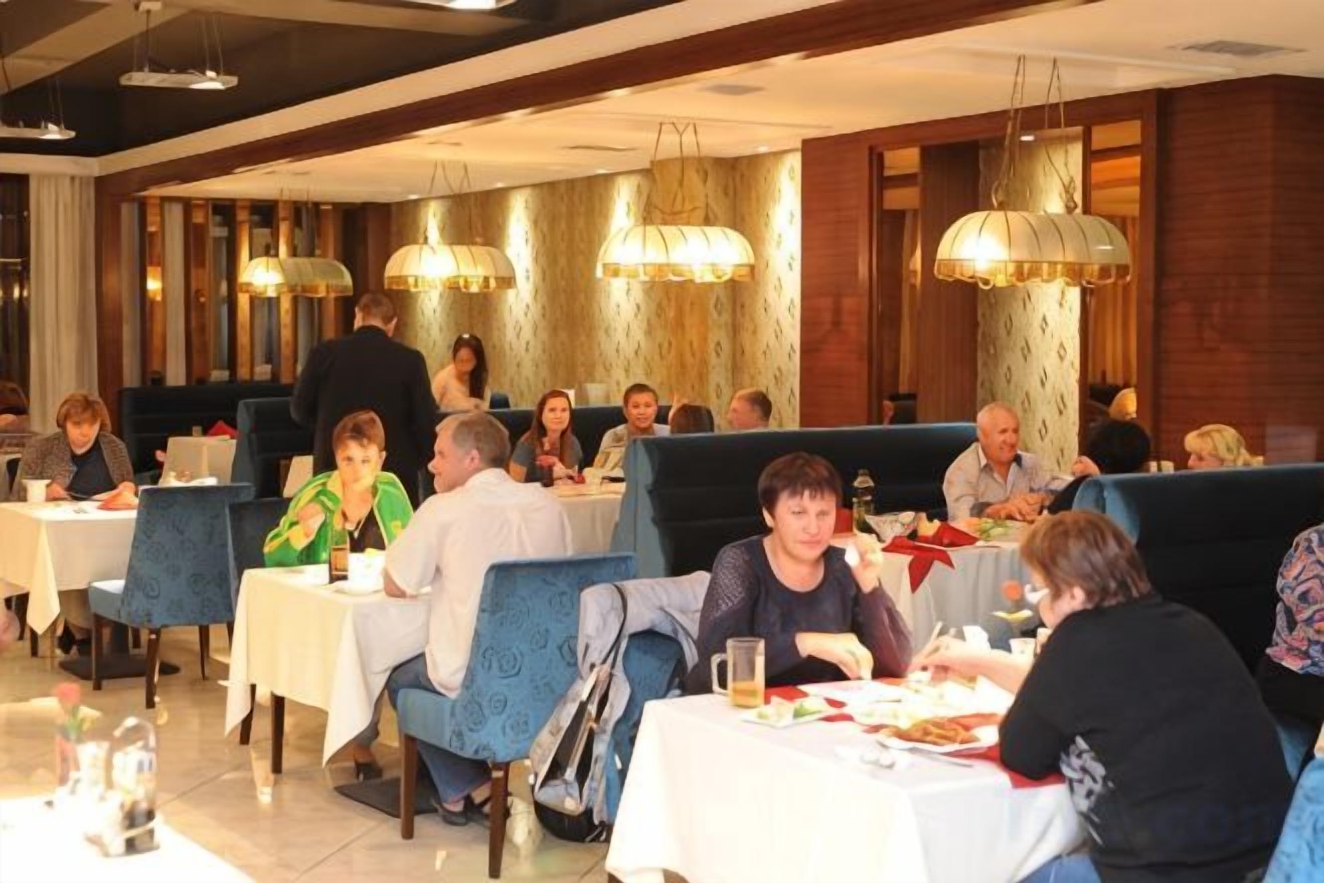 Un restaurante con varias mesas y cabinas, comensales cenando y un camarero al fondo.