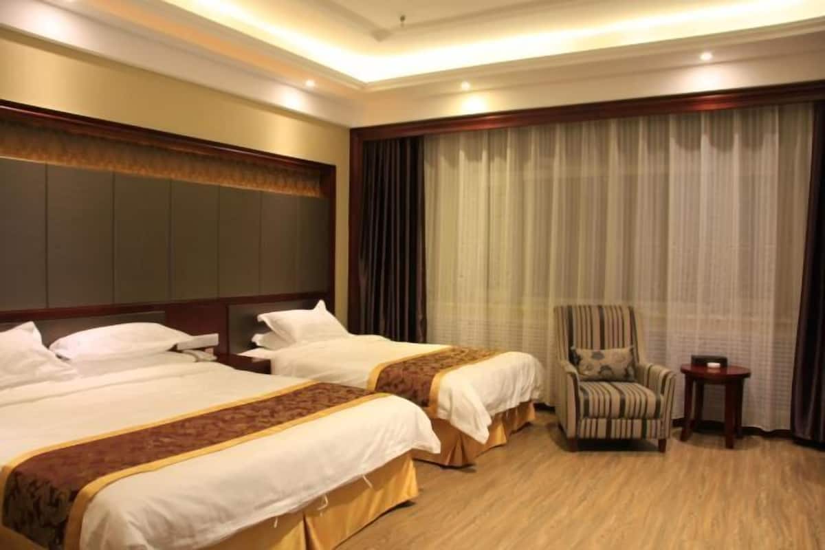 A hotel room with two beds, a chair, a small table, and a large window with curtains.