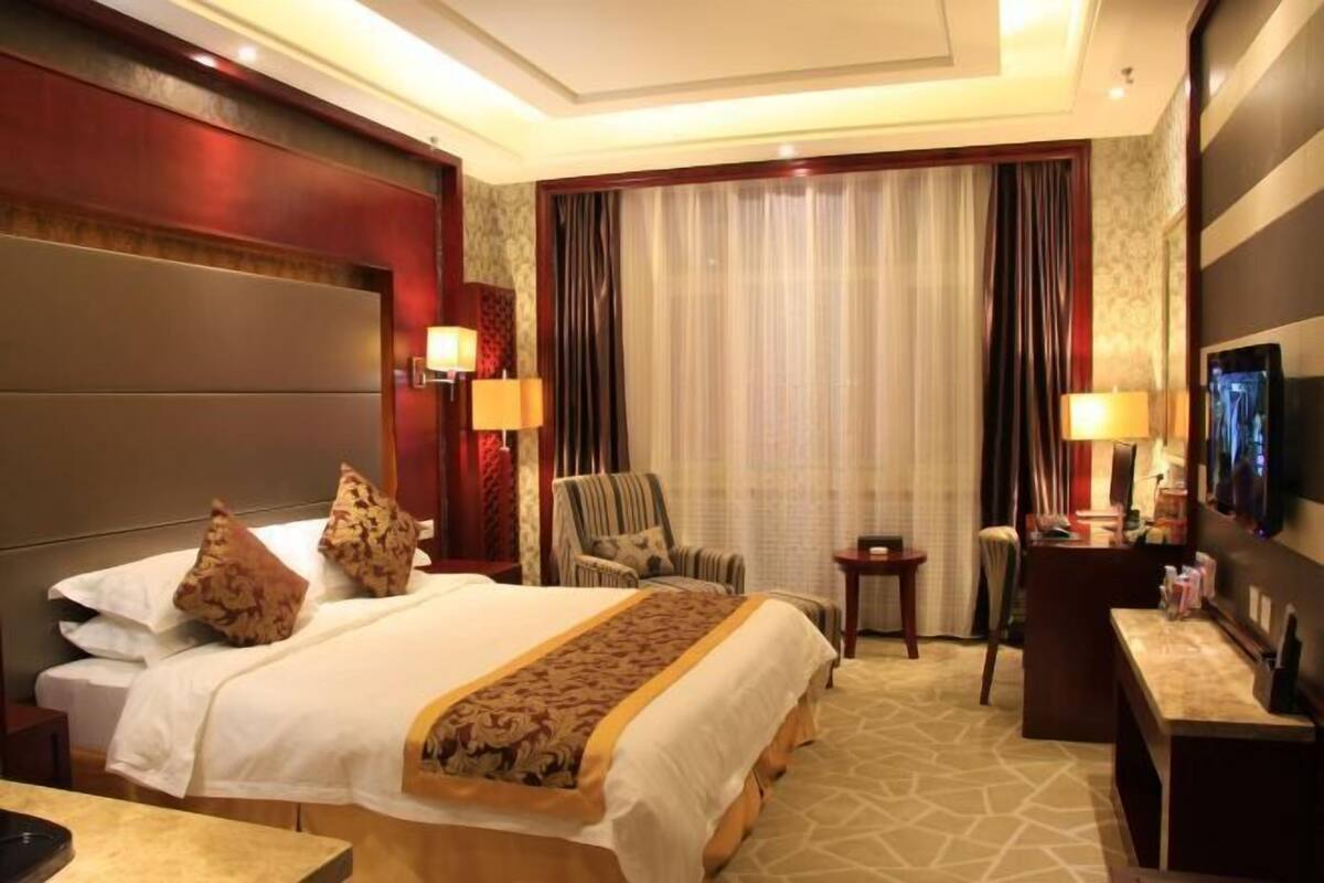 A hotel room with a large bed, a desk, a chair, a TV, and a window with curtains.