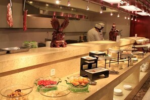 A buffet setup with various food items and a chef in the background. - Huilong Business Hotel (Fuyuan)