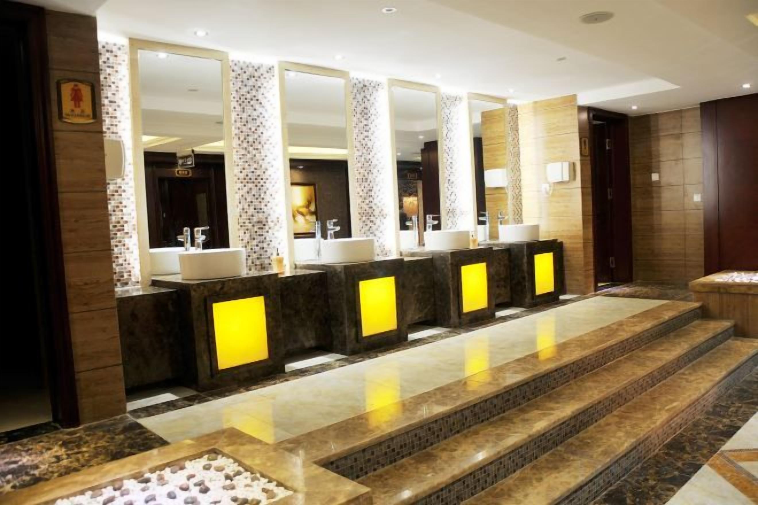 Des toilettes d’hôtel dotées de plusieurs lavabos, de miroirs et d’un sol carrelé.