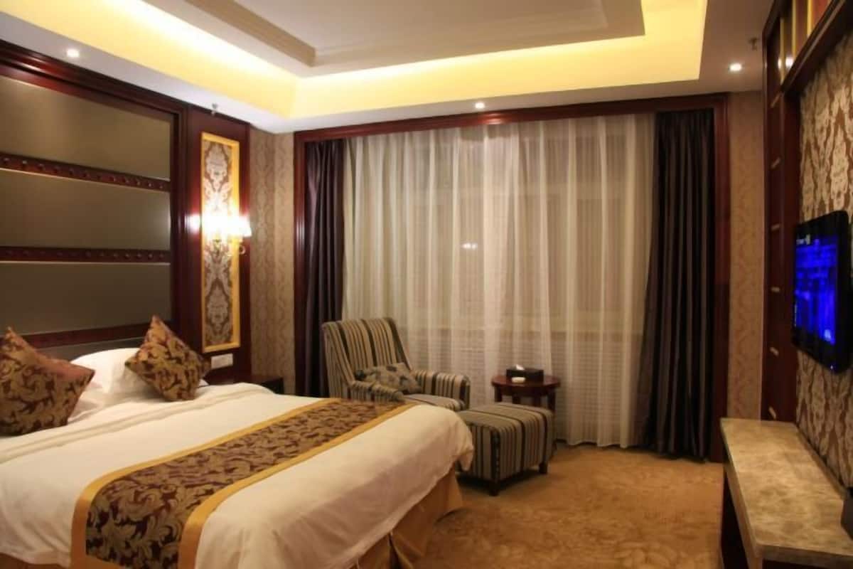 A hotel room with a large bed, a chair, a small table, a TV, and a curtain.