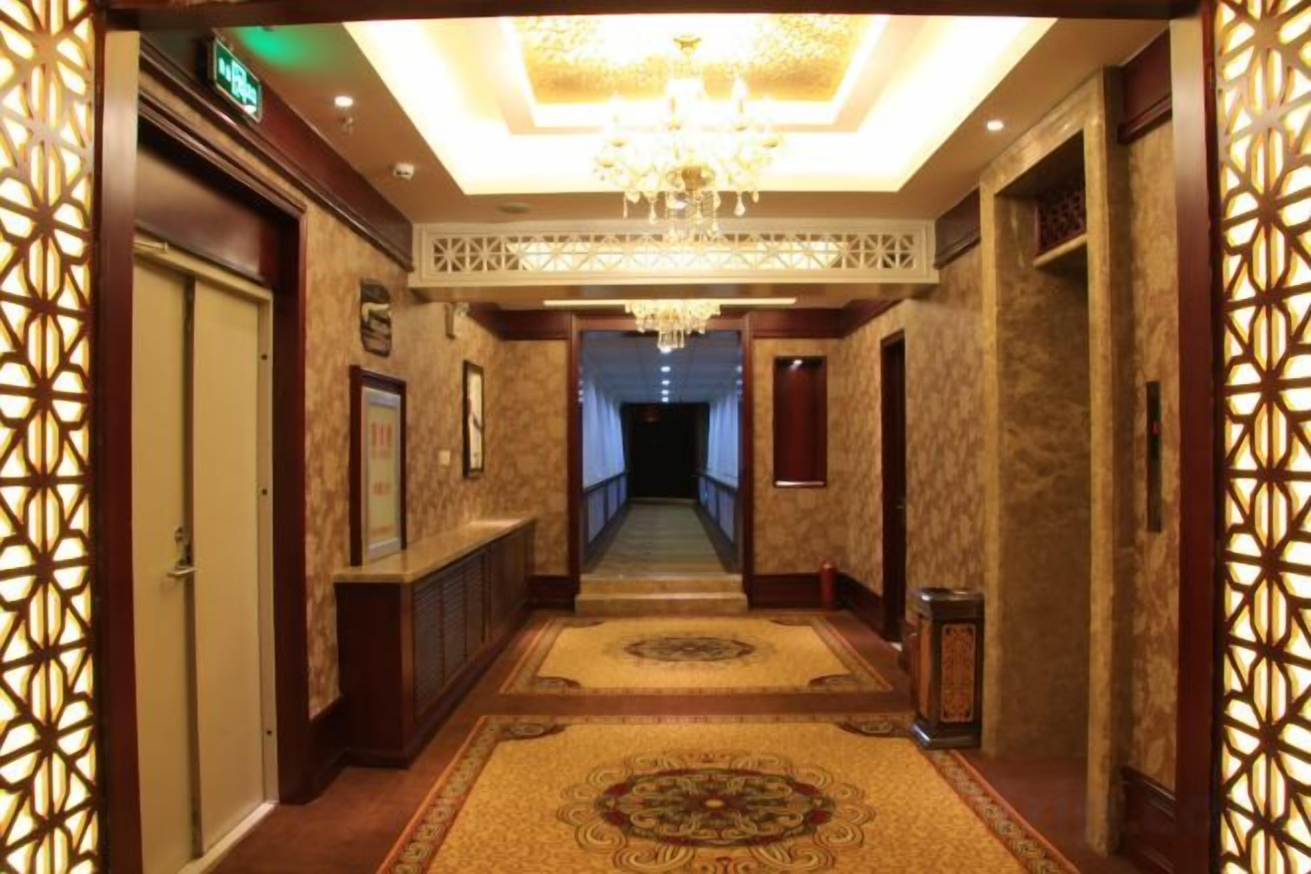 Un pasillo de hotel con candelabro, paredes con diseño y piso alfombrado.