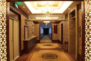 Un passadís d'hotel amb una làmpada de cristall, parets amb disseny i un terra amb moqueta.