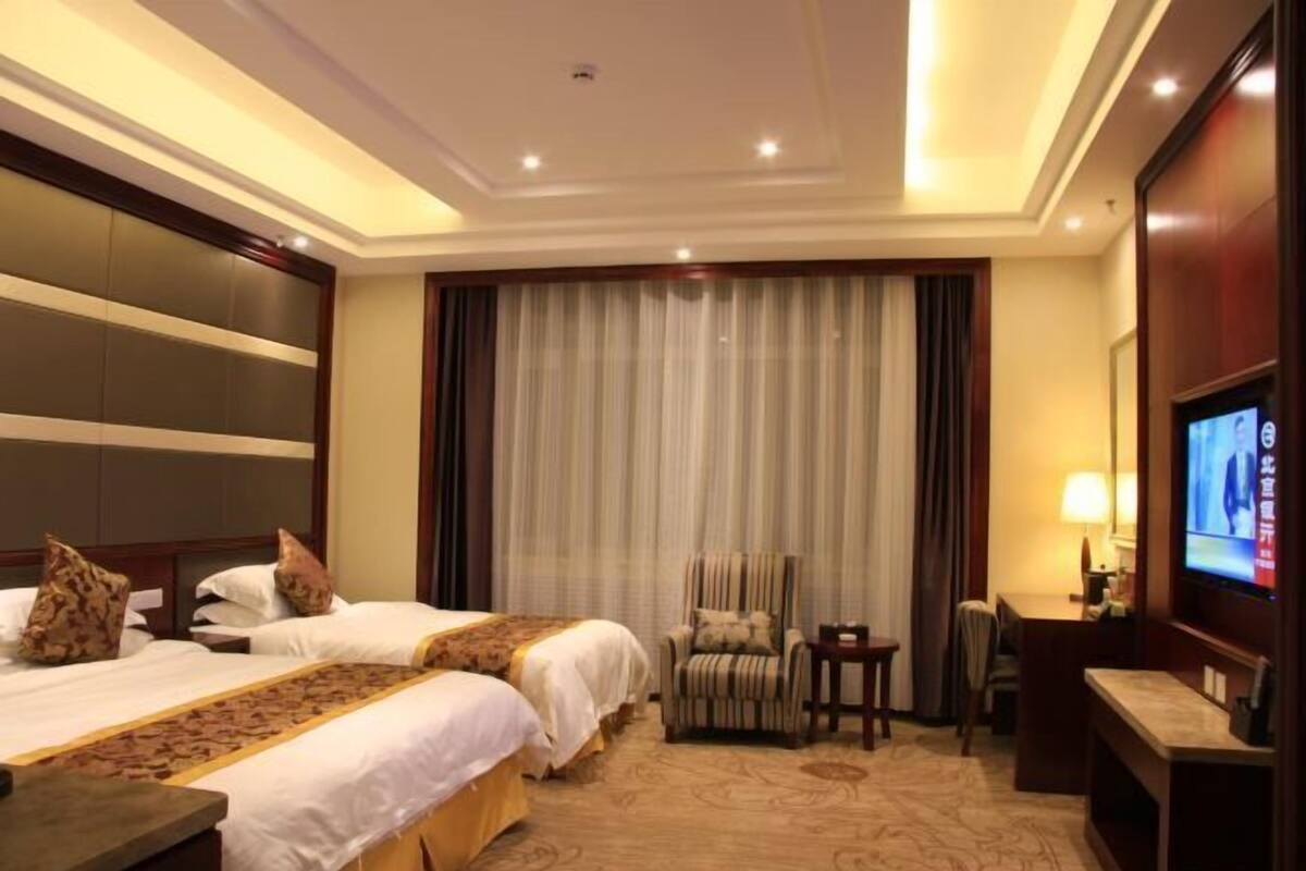 A hotel room with two beds, a TV, a desk, and a chair.