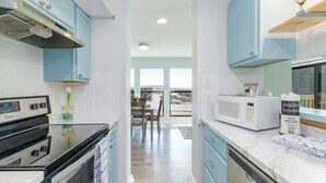 A modern kitchen with light blue cabinets, a black stove, and a white microwave. - Private & Comfy Oasis: 5-star, Ocean View, Pool, Near Golf ~ Free Parking! (Myrtle Beach)