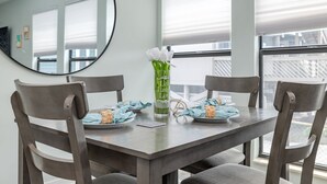 A dining table with four chairs, a vase with white flowers, and a glass bottle with text. - Private & Comfy Oasis: 5-star, Ocean View, Pool, Near Golf ~ Free Parking! (Myrtle Beach)