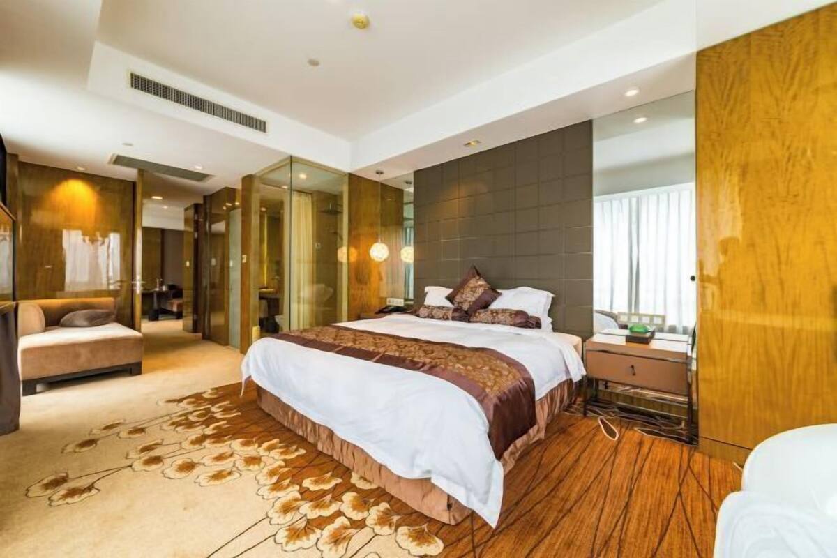 Ein modernes Hotelzimmer mit einem großen Bett, einer Couch, einem begehbaren Kleiderschrank und Blick auf die Stadt.