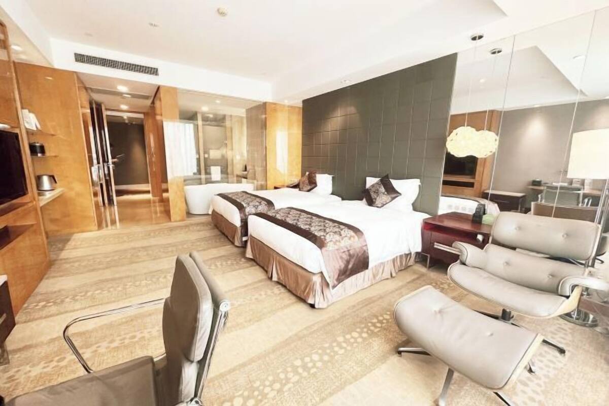 Ein Hotelzimmer mit einem großen Bett, zwei Nachttischen, einem Fernseher, einer Sitzecke mit Sessel und Sofa sowie einem Spiegel.
