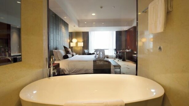 Una habitación de hotel moderna con una bañera grande, una cama con cabecera, un escritorio y una silla.