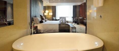 A modern hotel room with a large bathtub, a bed with a headboard, a desk, and a chair.