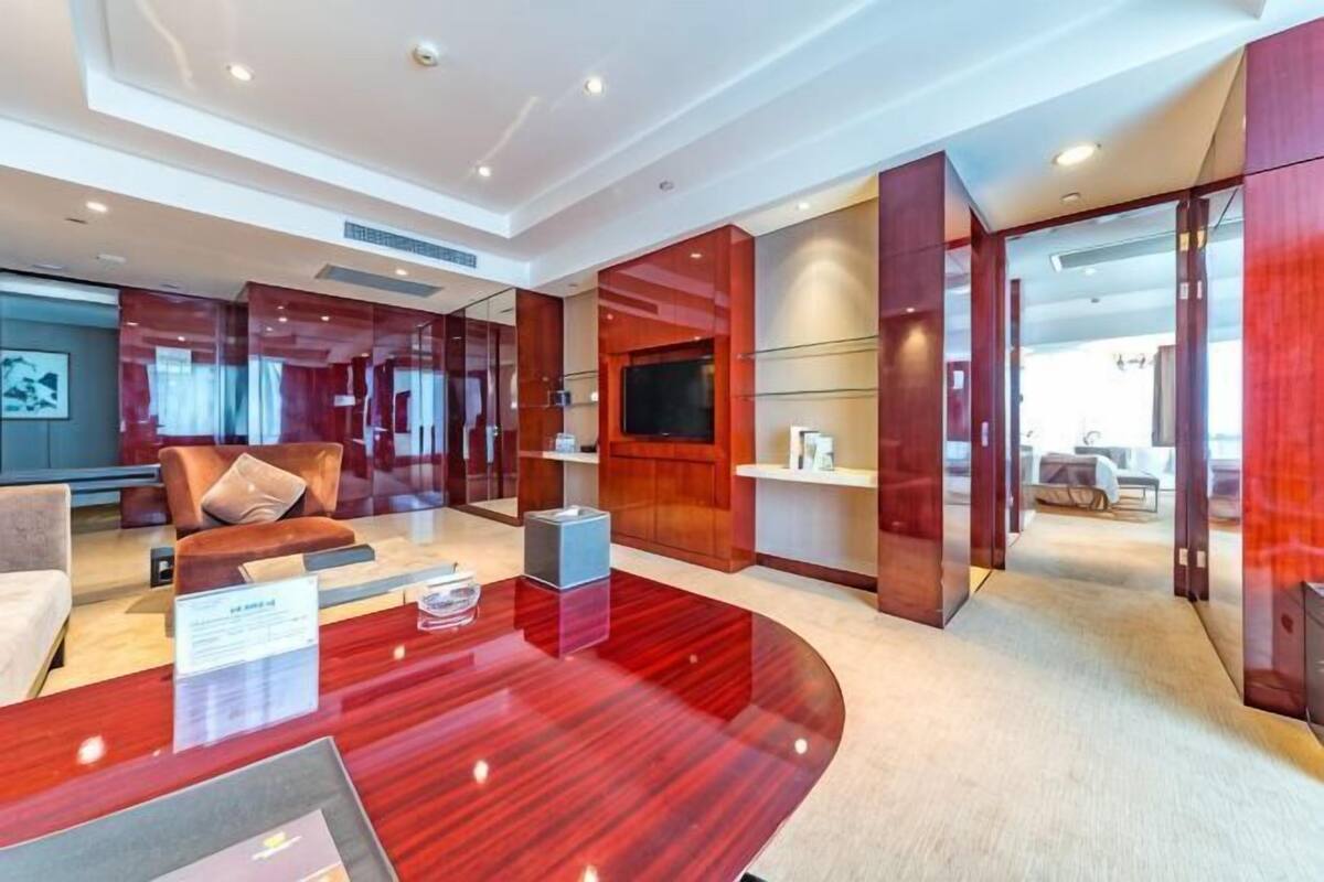 Eine moderne Hotellobby mit einer gebogenen Rezeption, einer Sitzecke mit Sofa und Sesseln, einem Fernseher und einem großen Fenster.
