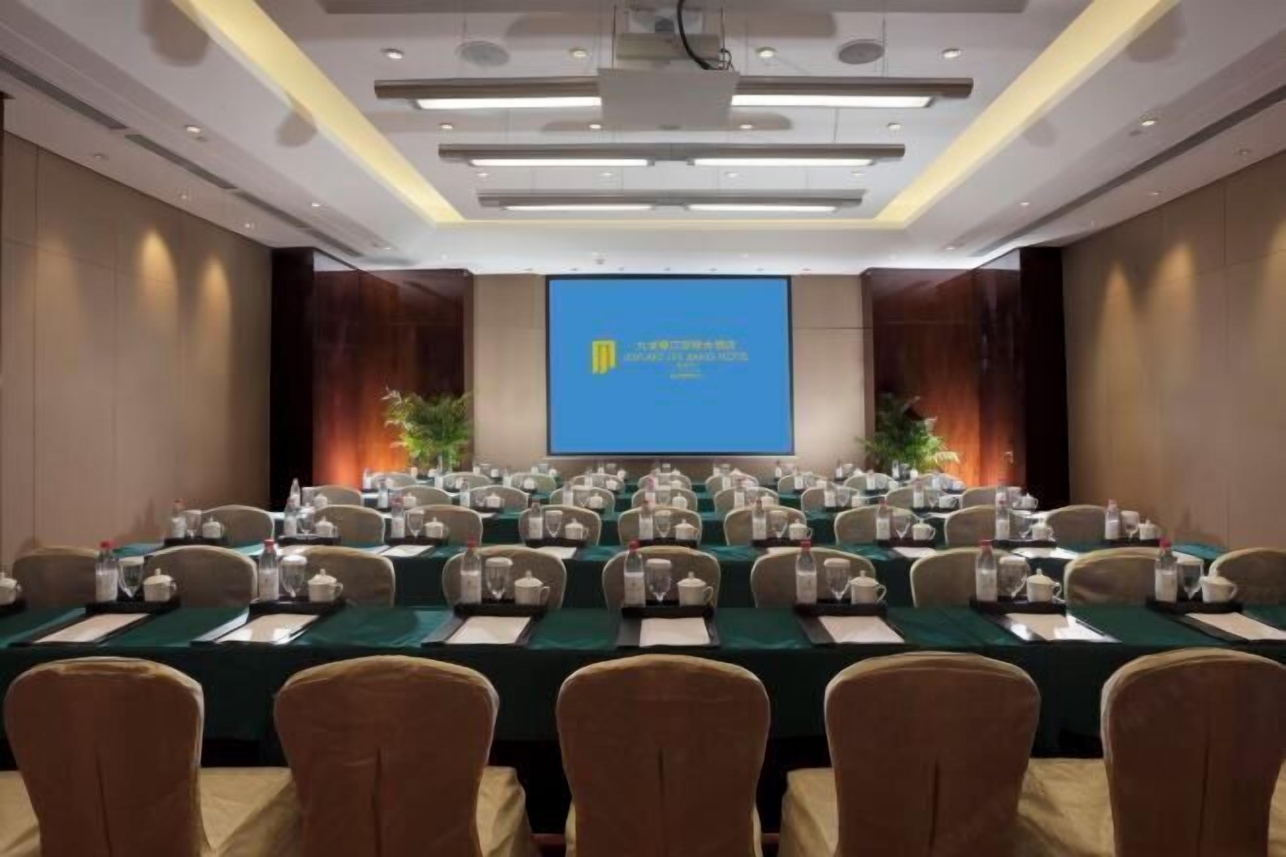 A conference room with a large screen at the front, multiple tables with chairs, and a projector.