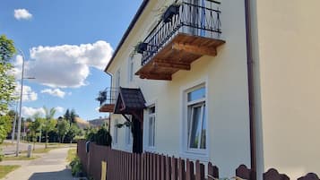 Un edificio de dos pisos con un balcón, una cerca de madera y un camino pavimentado.