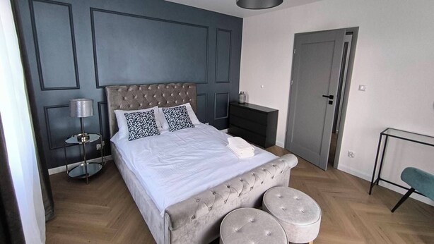 Une chambre à coucher avec un lit doté d’une tête de lit capitonnée, deux tables de chevet, une lampe de chevet et deux poufs.