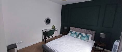 Un dormitorio con una cama grande, un escritorio y una silla. Hay una lámpara de pared y una lámpara de pie.