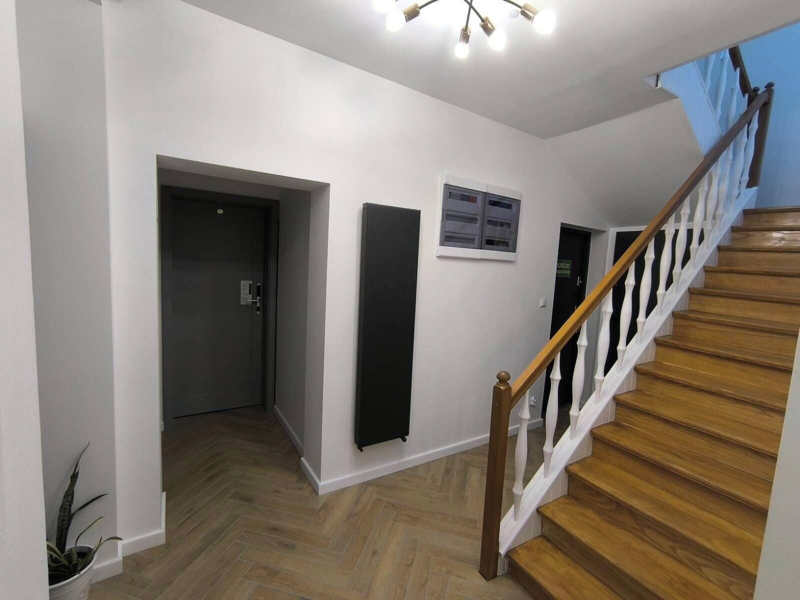 A hallway with a wooden staircase, a door with a sign, and a potted plant.