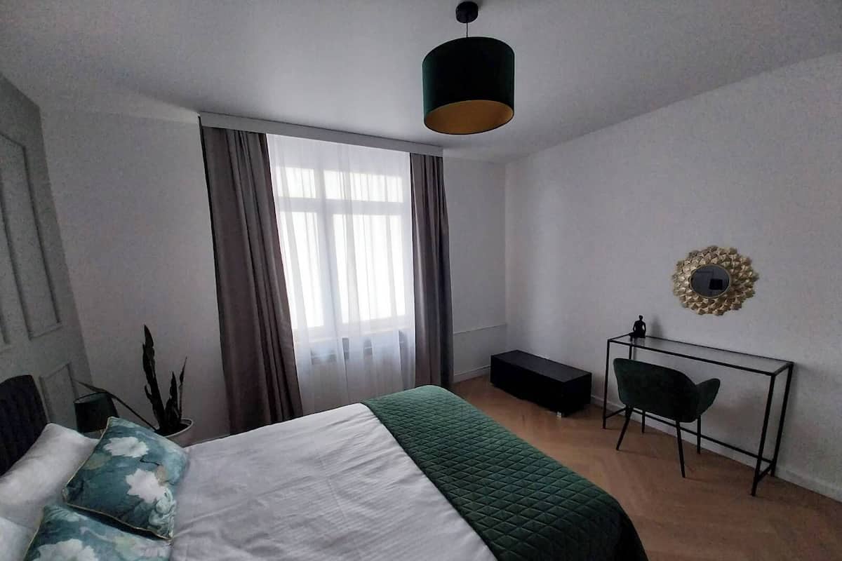 Un dormitorio con cama, escritorio, silla, una mesita y un espejo decorativo en la pared.