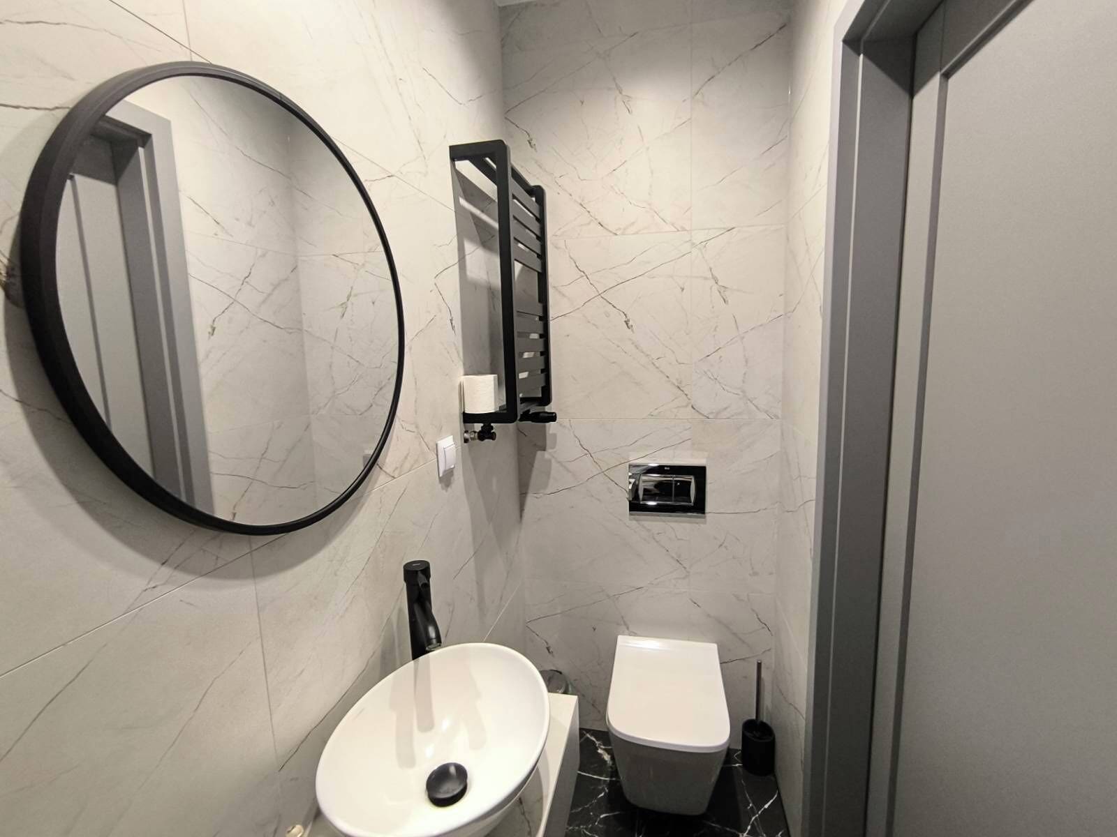 Un baño con un espejo redondo, un lavabo blanco, un inodoro y un perchero para toallas.