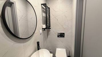 Un baño con un espejo redondo, un lavabo blanco, un inodoro y un perchero para toallas.