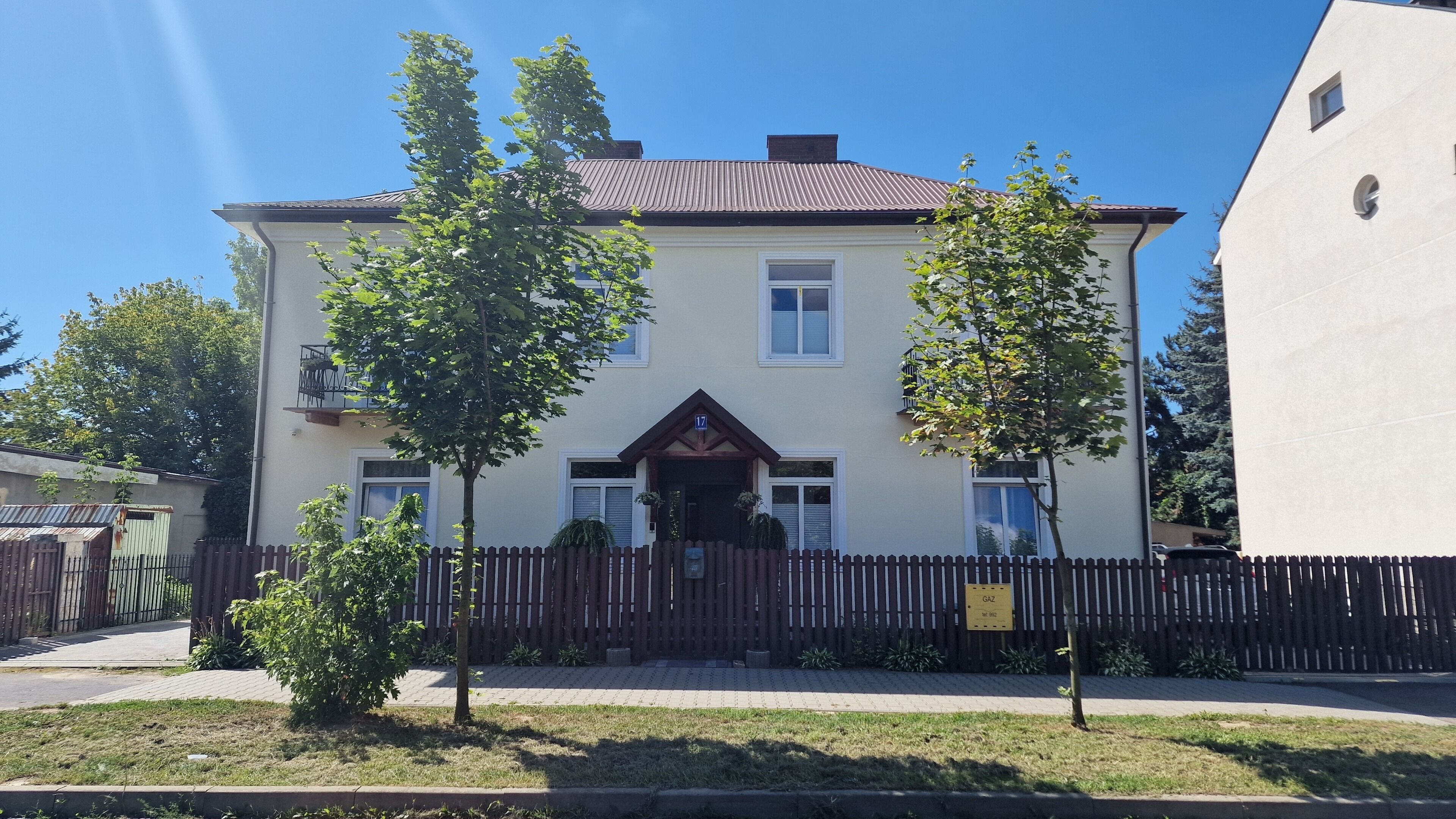 A two-story building with a brown roof, a number 17 sign, and a wooden fence in front.