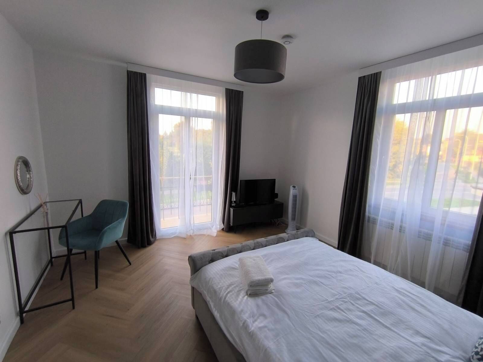 A bedroom with a bed, a desk, a chair, a TV, and a window with curtains.