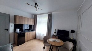 Un espace de vie compact comprenant un coin cuisine, un coin repas avec deux chaises, un téléviseur et un luminaire au plafond.