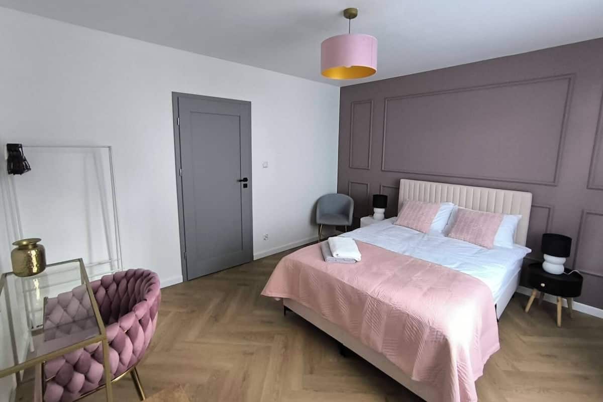 Un dormitorio con cama, una silla, una puerta y una lámpara colgante.