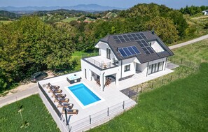 Een modern huis met twee verdiepingen, een zwembad, zonnepanelen en een prachtig uitzicht over het landschap.