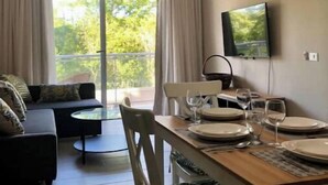 Un salon moderne avec un canapé, une table à manger pour quatre personnes et un téléviseur fixé au mur.