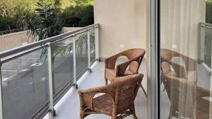 Un balcon avec des fauteuils en osier et une porte vitrée.