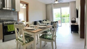 Une cuisine moderne équipée d’une cuisinière, d’un four et d’un ventilateur de plafond. On y trouve une table à manger avec des chaises, et un canapé à l’arrière-plan.
