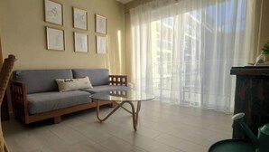 A living room with a sofa, a round coffee table, and a chair. There are framed pictures on the wall and a window with sheer curtains. - vr207h+c. Lovely apartment with pool view.

 (Bayahibe)