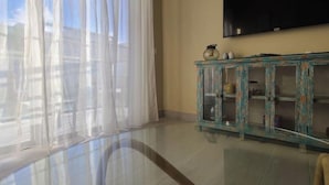 A room with a large window covered by sheer curtains, a flat-screen TV mounted on the wall, and a rustic wooden cabinet with glass doors. - vr207h+c. Lovely apartment with pool view.

 (Bayahibe)